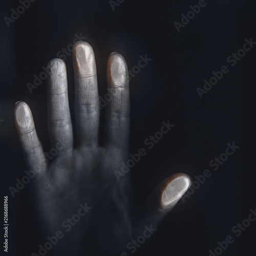 Raised human hand glowing faintly against dark background, mysterious moody spiritual gesture portrait