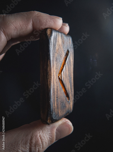 Hand holding carved wooden Kenaz rune symbol close-up, mystical divination tool detail macro