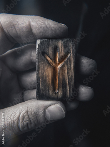 Hand holding carved wooden Elhaz rune symbol, close-up mystical divination tool detail