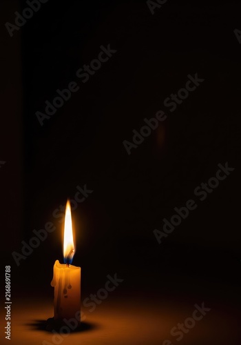 A single golden candle flame flickers gently in a vast dark room, casting a warm and peaceful glow that represents hope and quiet serenity, atmosphere, faith, yellow