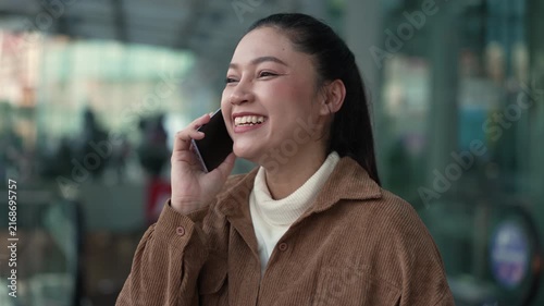 happy woman talking on a smartphone while standing near an escalator in the shopping mall or department store