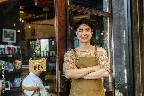 Foto Young barista cafe owner smiling at entrance with open sign visible, confident entrepreneur representing hospitality service and customer readiness, positive mood in small business operation