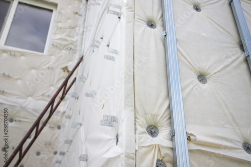 low-angle view of a house under renovation with exterior insulation membrane, fasteners, metal battens and window, documenting energy retrofit before final cladding