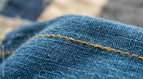 Close-up view of blue denim fabric with detailed yellow stitching, showcasing woven texture and garment construction