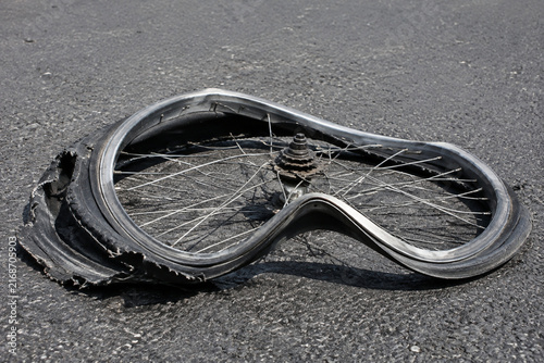 Mangled bicycle wheel on asphalt with bent rim and tangled spokes, bicycle accident and damage concept