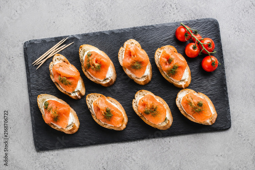 Toasted bread with cream cheese and smoked salmon on slate board with cherry tomatoes, appetizer concept