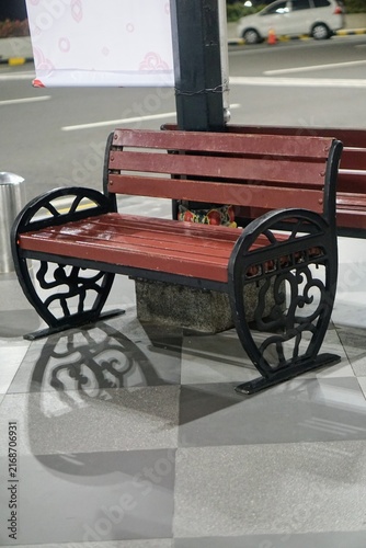 Classic antique style public seating featuring red wood slats and unique shadow cast on tiled floor.