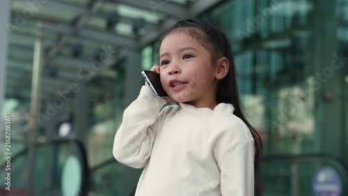 happy child girl talking on a smartphone while standing near an escalator in the shopping mall or department store