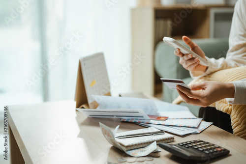Budget review shows a woman using a smartphone and card among bills and a calculator, linking finance choices, savings, and household expenses for commercial use. Credit card, debt; credit focus.