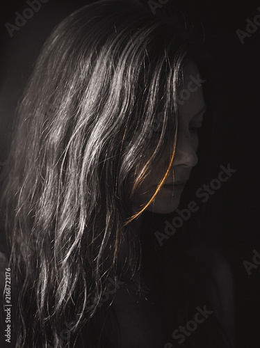 Woman with long hair in profile, warm rim light against dark background, moody portrait