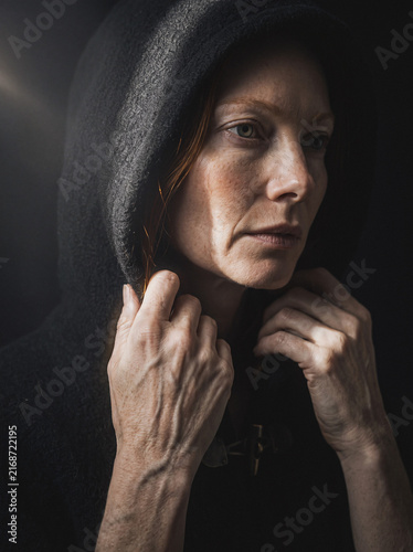 Hooded woman looking sideways in moody dramatic light, mysterious contemplative portrait