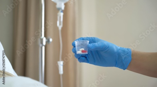 Gloved hand holding cup of pills beside iv stand for hospice and palliative care medication administration background and healthcare brochure design