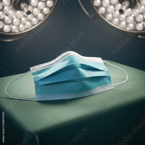 Sterile blue surgical mask resting on a green cloth in a brightly lit operating room with surgical lights above