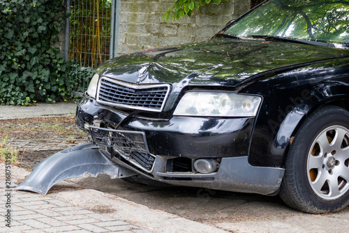 Foto Damaged black sedan with broken bumper and smashed hood after road collision par