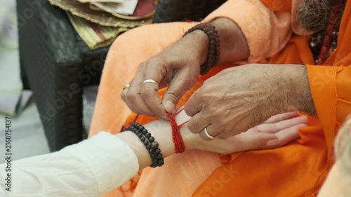 hindu monk tying sacred red thread on devotee wrist during spiritual ceremony. holy thread brings divine protection and positive karma to believer. tying thread is tradition for spiritual blessing