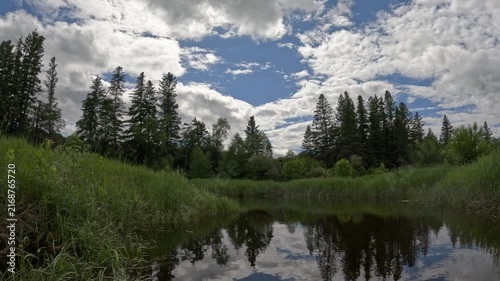 POV from the front of a canoe moving along a calm narrow stream surrounded by nature

