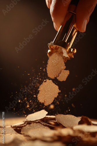 truffle luxury cuisine concept. Close-up of hand holding knife slicing through wood, shavings flying in kitchen setting with blurred background elements