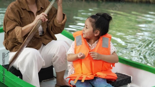 slow motion of happy mother and preschool child girl in a green paddle boat on a scenic pond.