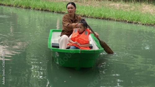 slow motion of happy mother and preschool child girl in a green paddle boat on a scenic pond.