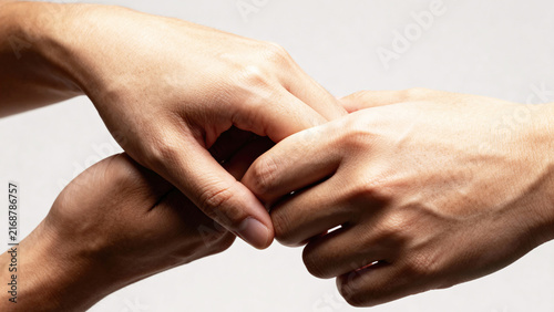 Two hands of different skin tones gently clasping each other against a neutral background, symbolizing unity and connection between diverse individuals. Physicality, tactility