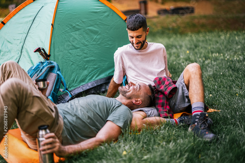 Gay couple sitting together and laughing beside their camping tent