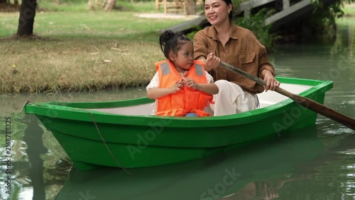 slow motion of happy mother and preschool child girl in a green paddle boat on a scenic pond.