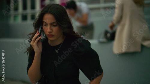 A young business woman is deeply engaged in a phone conversation outdoors. She appears focused and serious while talking on her mobile phone in an urban environment.