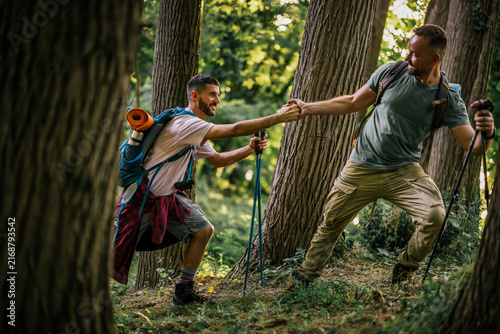 Two hikers helping each other navigate uneven terrain in a forest