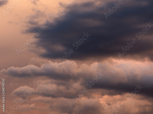 Dramatic dark storm clouds illuminated by warm orange sunset light, creating a moody atmospheric cloudscape before a possible thunderstorm.