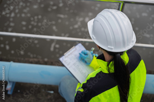 Environmental engineer inspects a water treatment basin and records operational data. Concept of wastewater treatment, water management, environmental monitoring, and utility operations.