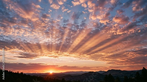 Golden sunset over mountain ridge with scattered clouds and warm crepuscular sun rays radiating across dramatic orange and pink twilight sky at dusk