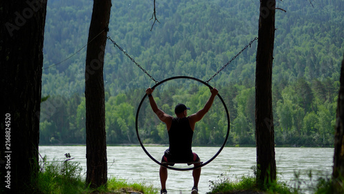 Cuadro en lienzo Sequential shot of a young man relaxing on a round ring swing and raising his hands to grab the edge while looking at the majestic Siberian mountains