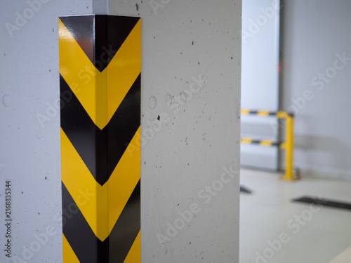 Black and yellow hazard stripes on a protective corner guard attached to a concrete pillar in a parking garage. Industrial safety marking and collision protection detail.