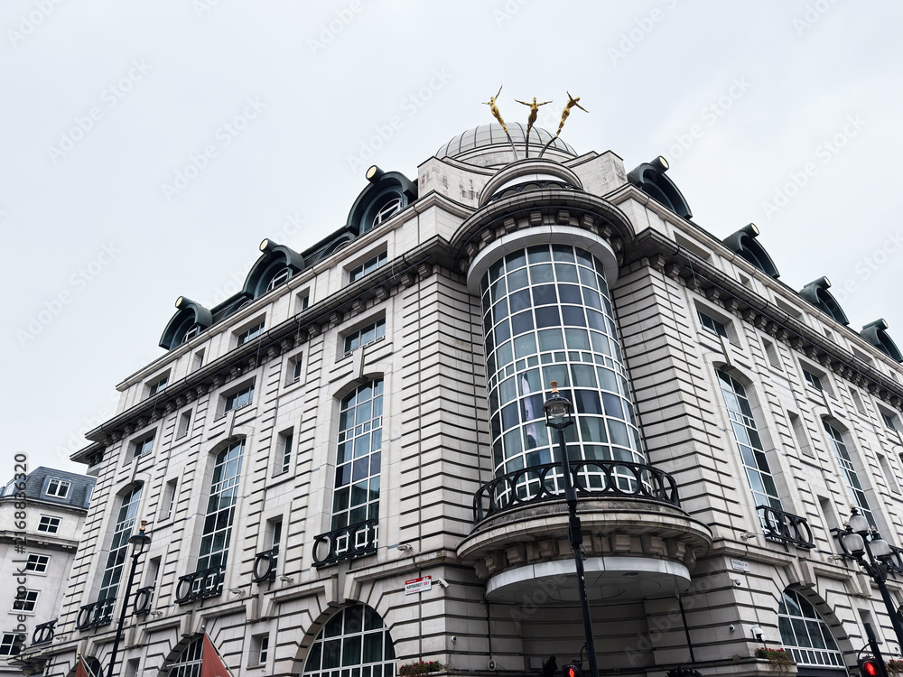 Obraz premium Historic commercial building with grand curved glass bay and classical architecture in London, UK, elegant stone facade and rooftop sculptures against a pale sky