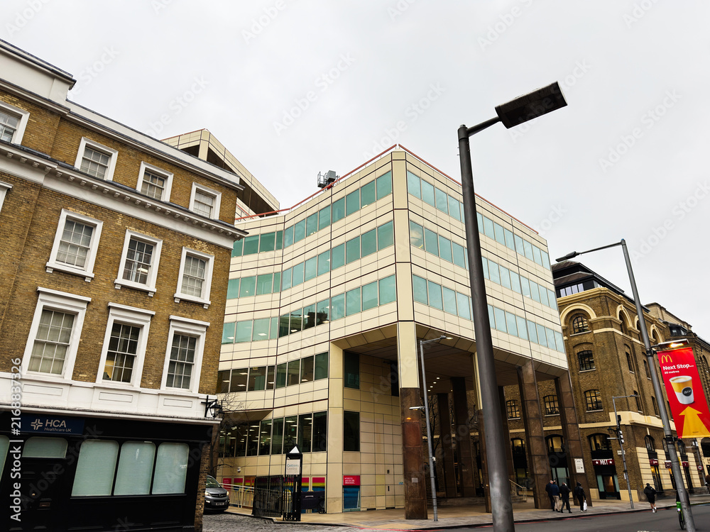Obraz premium Modern Cottons Centre office building and historic brick facades on a busy London, UK street with pedestrians, street lamps and urban architecture