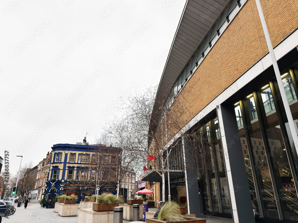 Obraz premium Modern city street with contemporary office building and historic pub facade, pedestrians and planters in London, UK on an overcast winter day