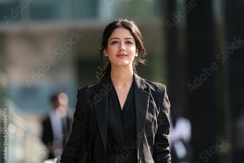 Stylish young businesswoman in a black blazer walking outside a modern office building