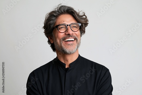 Cheerful middle-aged man with glasses laughing against a light studio background