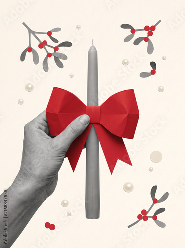 Christmas candle with red bow held by grayscale hand beneath mistletoe and floating ornaments