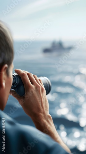 Person observing a distant ship over sparkling ocean waters through binoculars on a bright and clear day