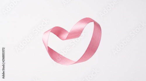 A pink breast cancer awareness ribbon forming a subtle heart-like shape, symbolizing a mother's love and support, isolated alone on a completely plain white background, elegant satin material, soft 