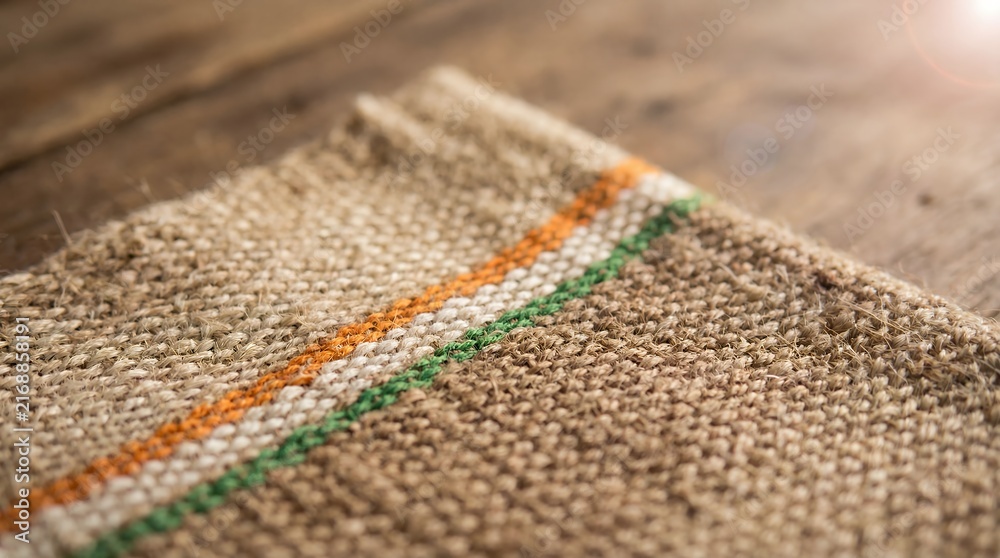 Fototapeta premium Rustic Jute Burlap Fabric with Orange, White and Green Stripes on Wooden Table, Natural Textile Background for Indian Craft, Eco Packaging and Sustainable Design