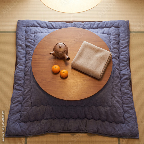 Overhead view of a cozy Japanese kotatsu table with quilted blanket, teapot, mandarin oranges and folded wool throw