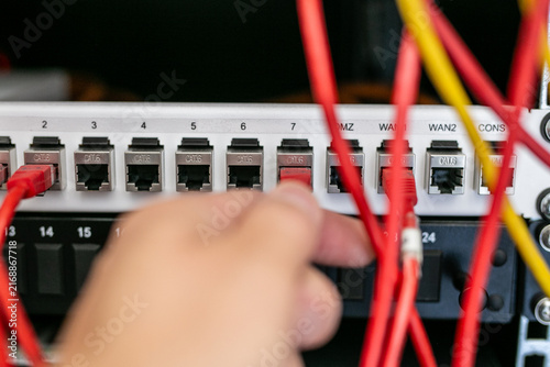 Quadro su tela Close-up of a person's hand plugging an Ethernet patch cable into a numbered network port on a patch panel or network switch inside a server rack