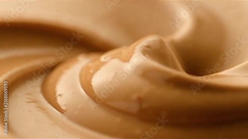 Thick peanut cream with roasted nut pieces forms glossy waves in a premium ultra-macro food background.