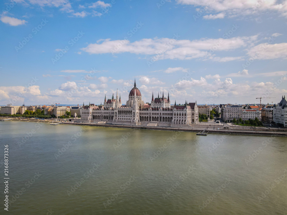 Fototapeta premium Hungarian Parliament Building and Danube River under a Bright Blue Sky with White Clouds