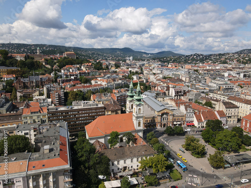 Aerial view of a city with historical buildings, houses, and green hills under cloudy sky