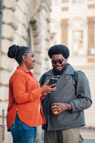 Fotografie Young diverse couple looking at a mobile phone screen on a city street, sharing