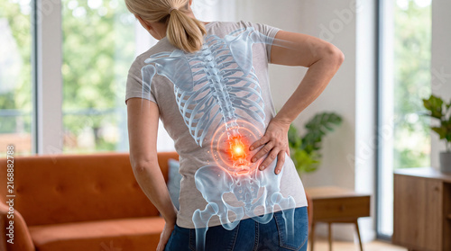 Woman holding lower back with glowing spine skeleton overlay highlighting lumbar pain at home