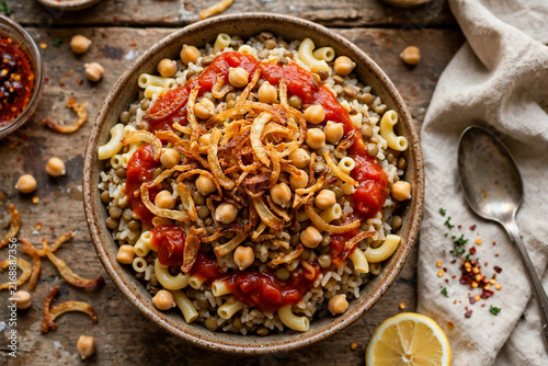 egyptian koshari bowl traditional rice lentils pasta chickpeas fried onions tomato sauce overhead rustic table authentic street food